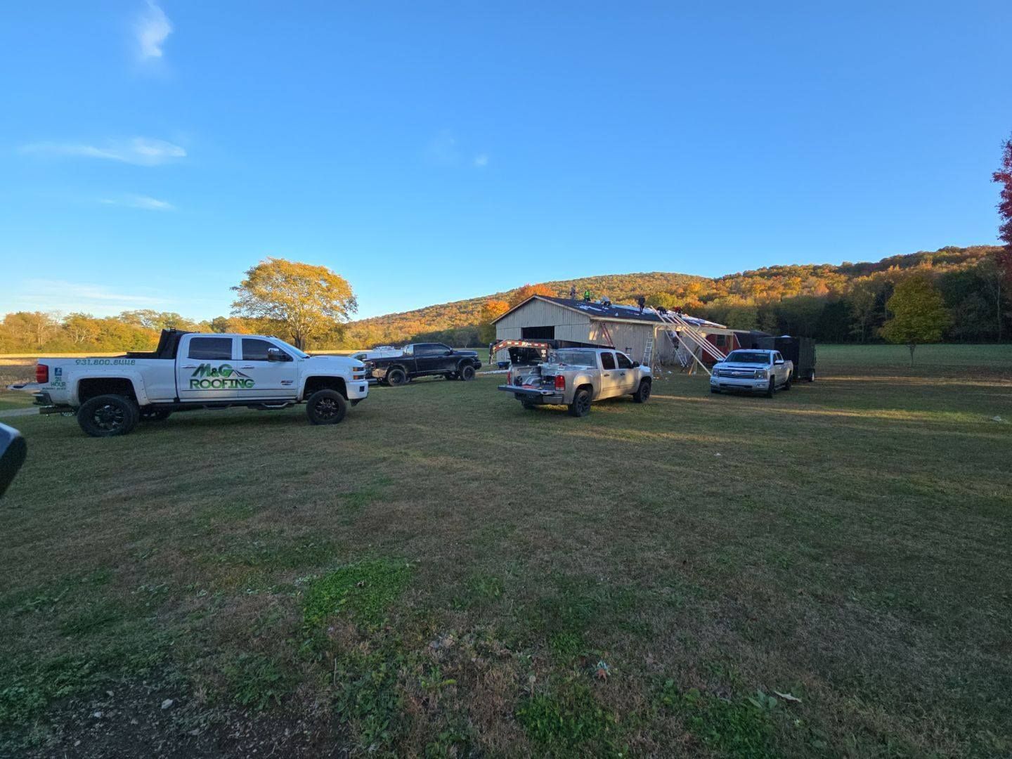 Several trucks parked on a grassy field near a barn under a blue sky.