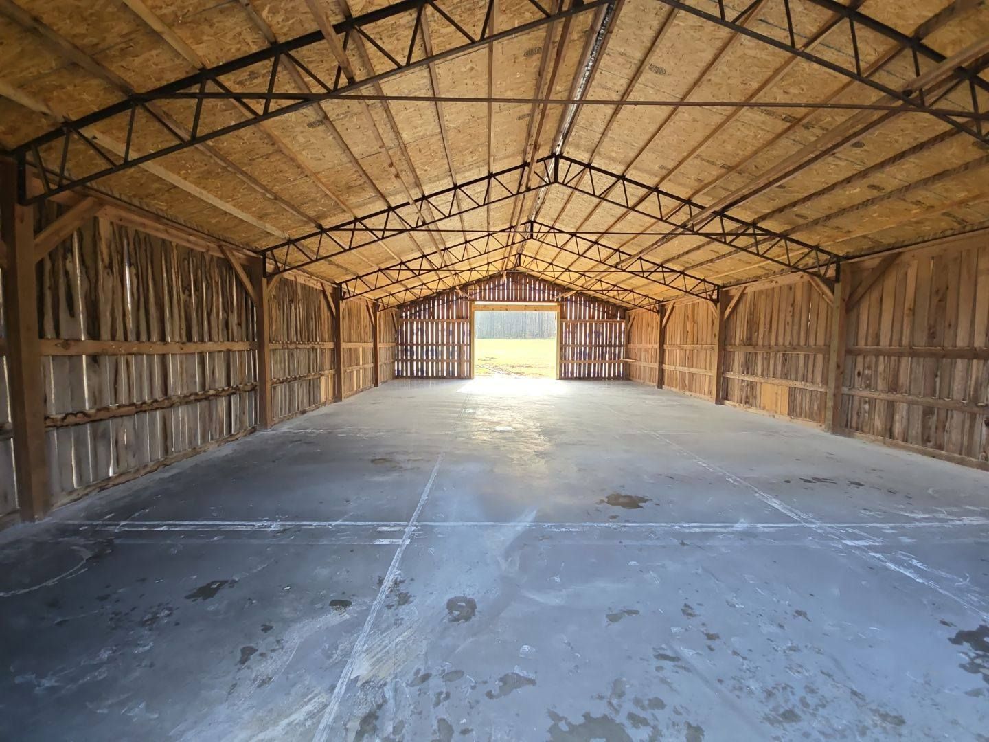 Interior of a large empty barn with a concrete floor, wooden walls, and open doorway, flooded with light.