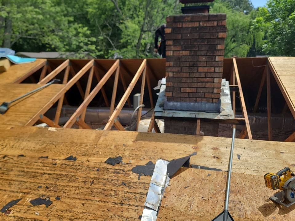 Roof construction with exposed wooden rafters, brick chimney, and partially covered with plywood.