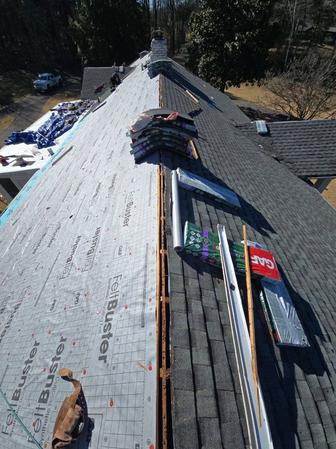 Roof partially covered with old and new asphalt shingles. Roofing materials and tools on site.
