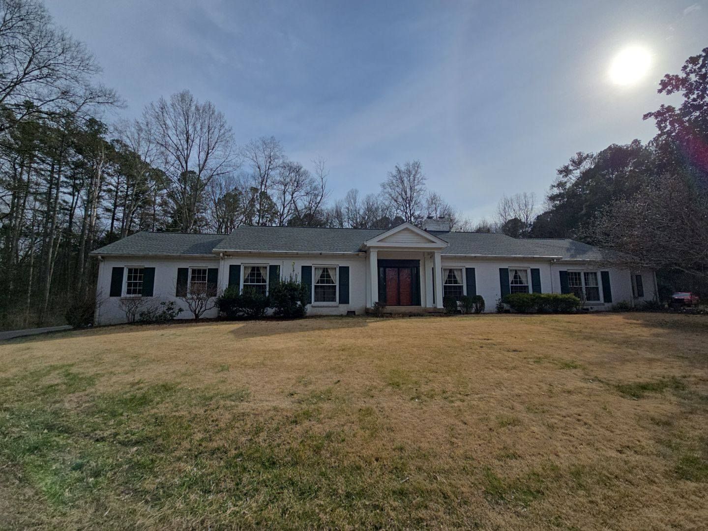 White one-story house with green shutters, double red front doors, and a grassy yard under a sunny sky.