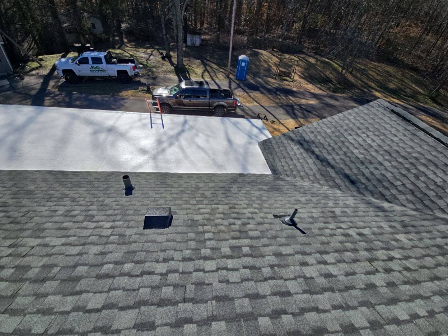 Roof with dark grey shingles, looking at construction area with trucks and a concrete pad.