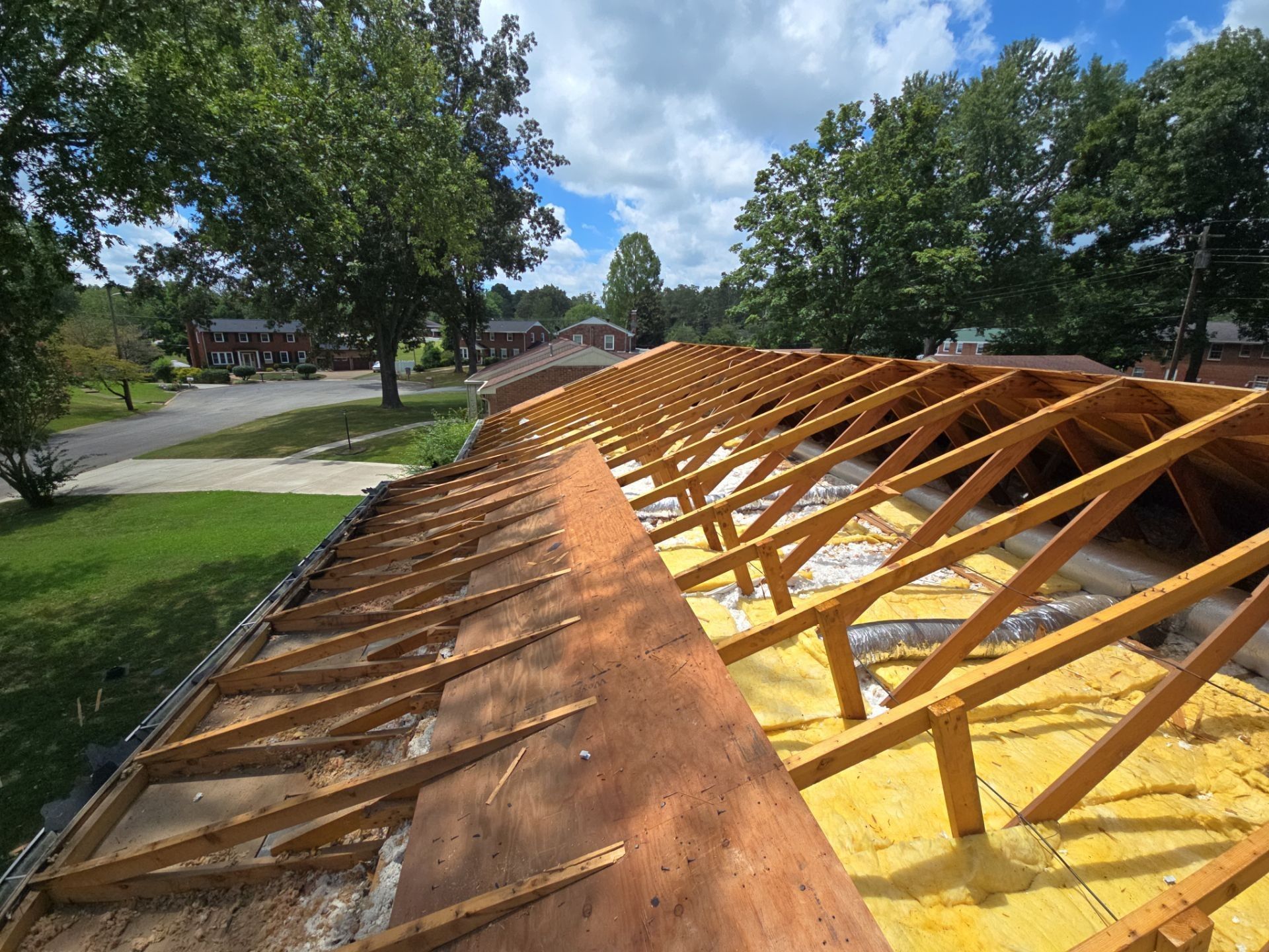 Roof under construction: exposed wooden beams, insulation, and partial sheathing. Sunny day.