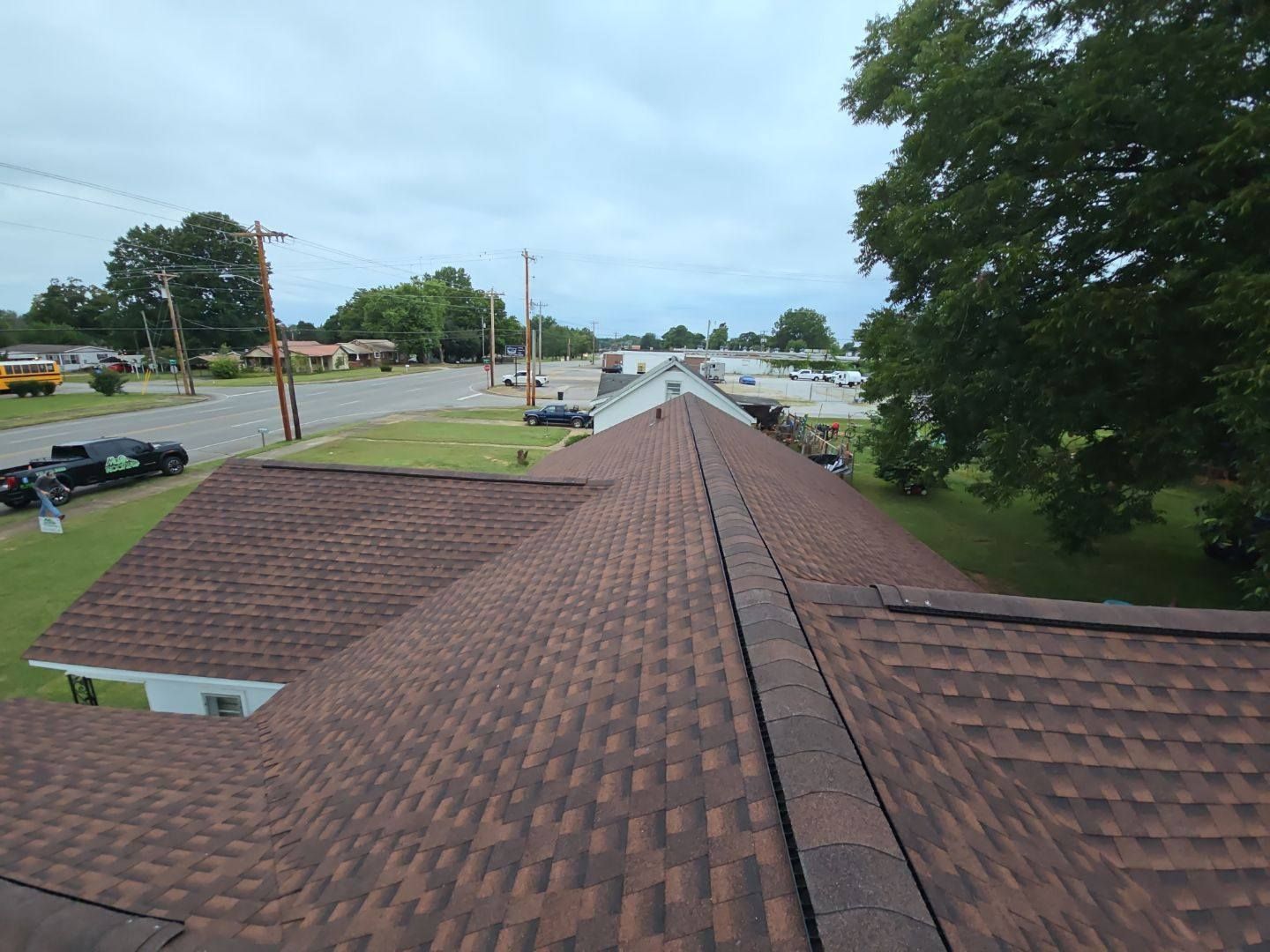 Brown shingled roof, trees, and street under a cloudy sky.