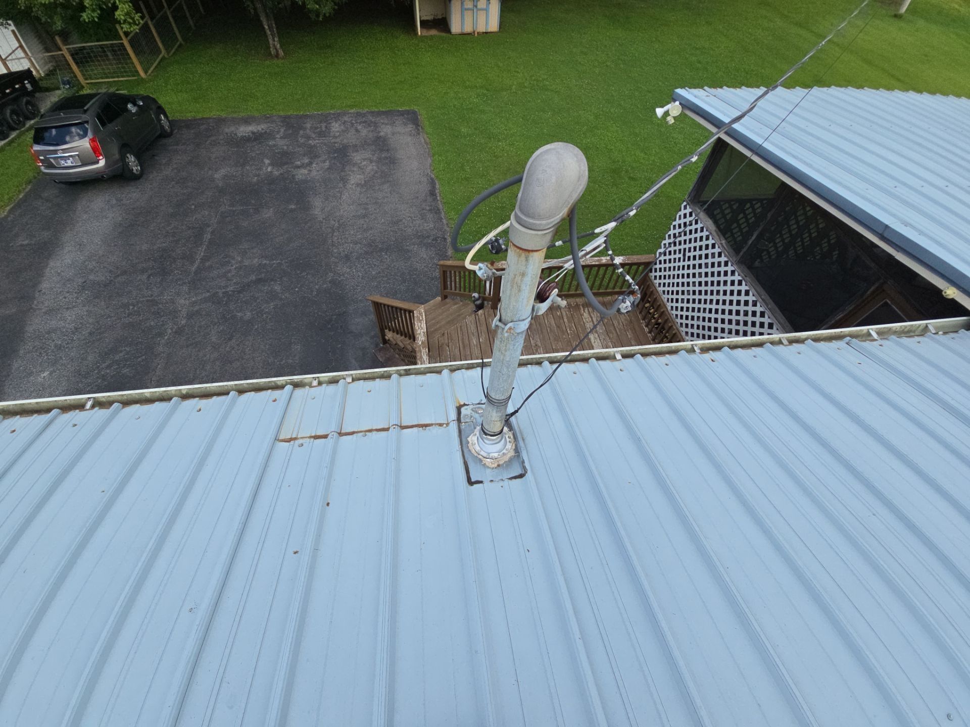 Gray metal roof with a vent pipe and attached wires. A car sits in the driveway.
