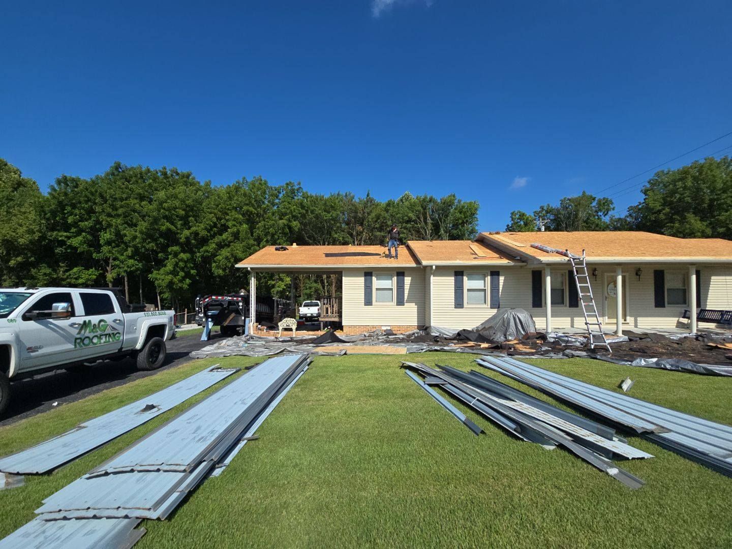 Roofing work in progress on a one-story house with a truck parked in the yard; blue sky.