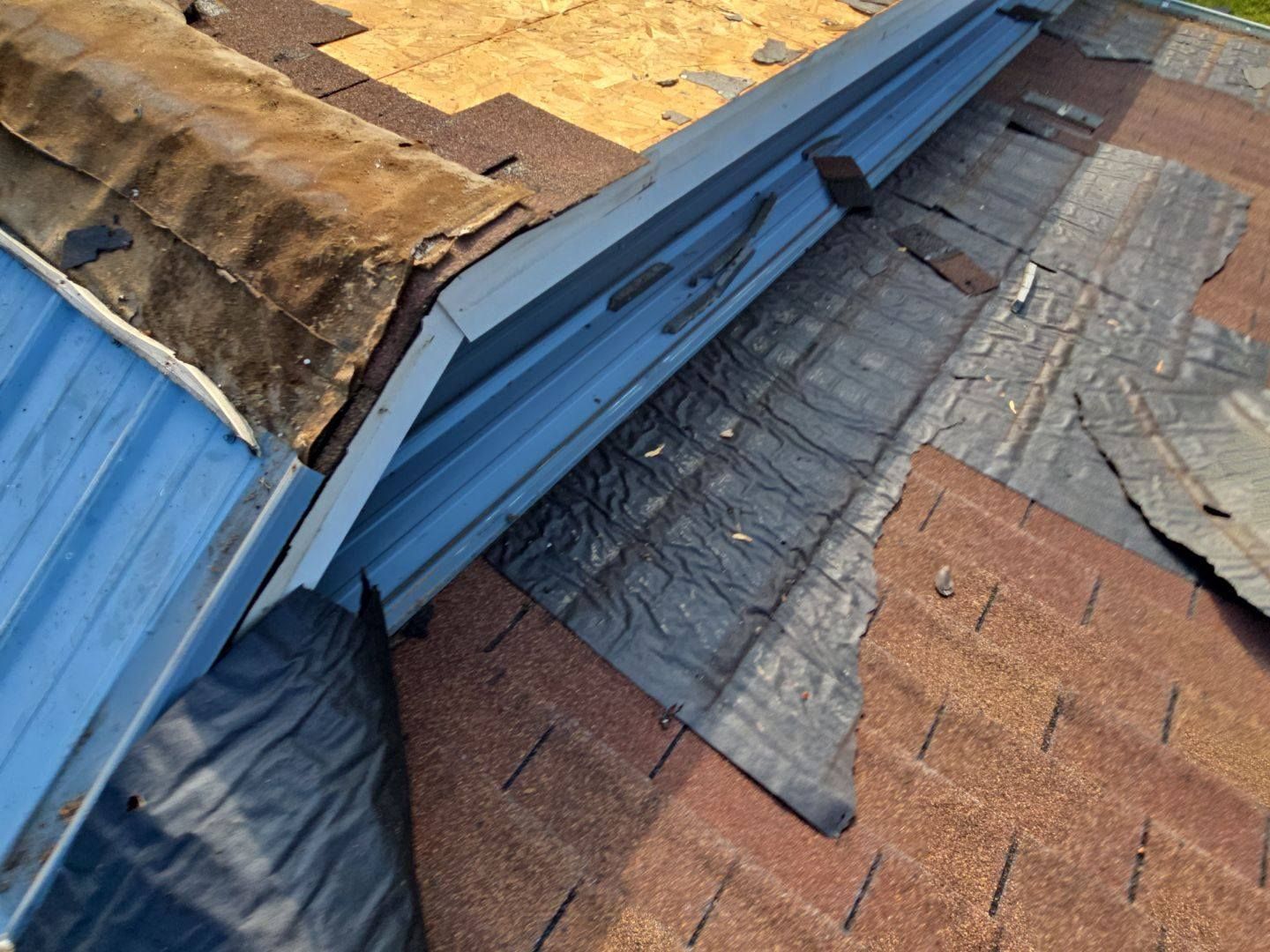 Damaged roof with peeling shingles, metal flashing, and partial covering.