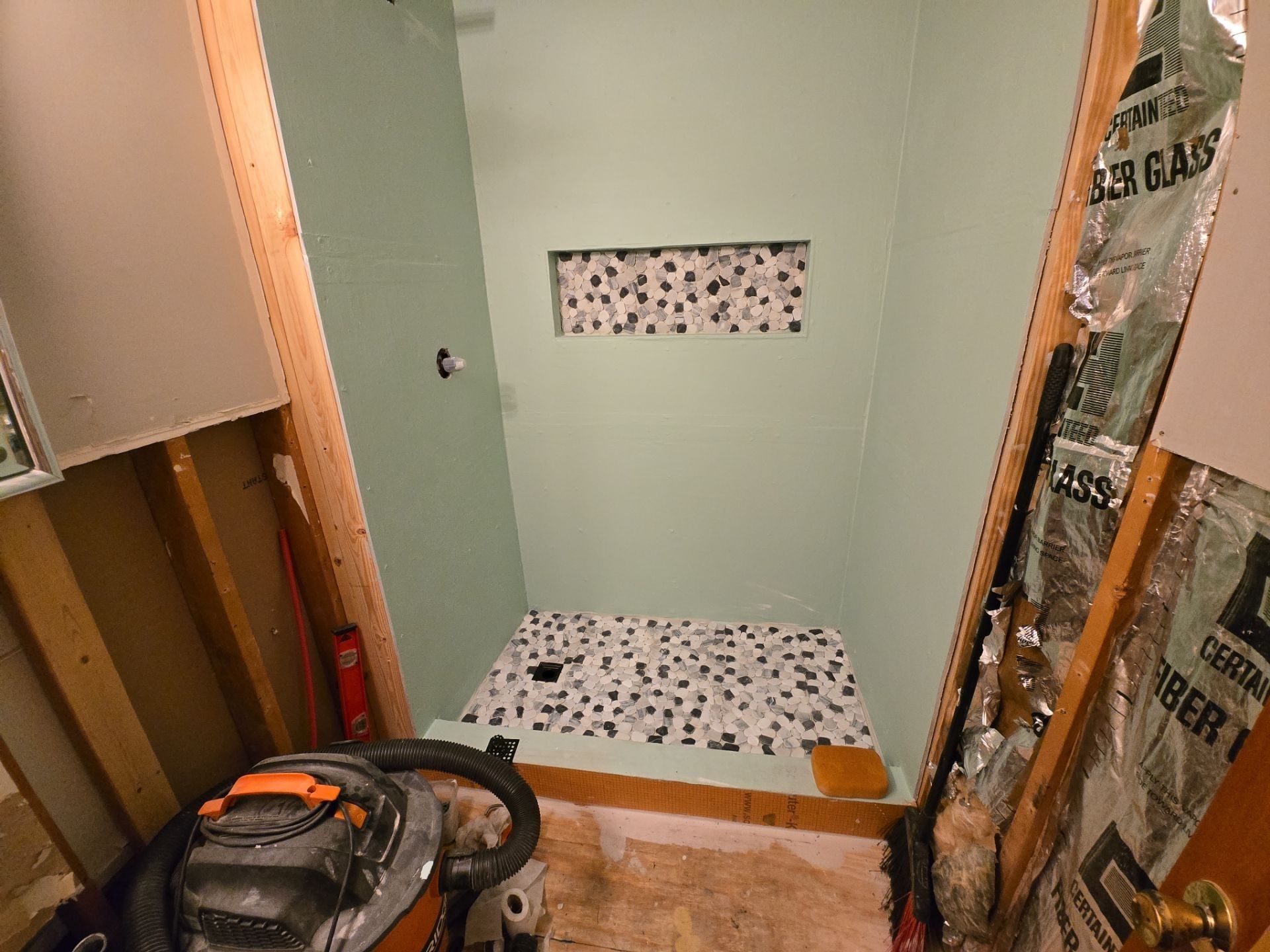 Bathroom under renovation with light green walls, mosaic tile floor, and a built-in shelf.