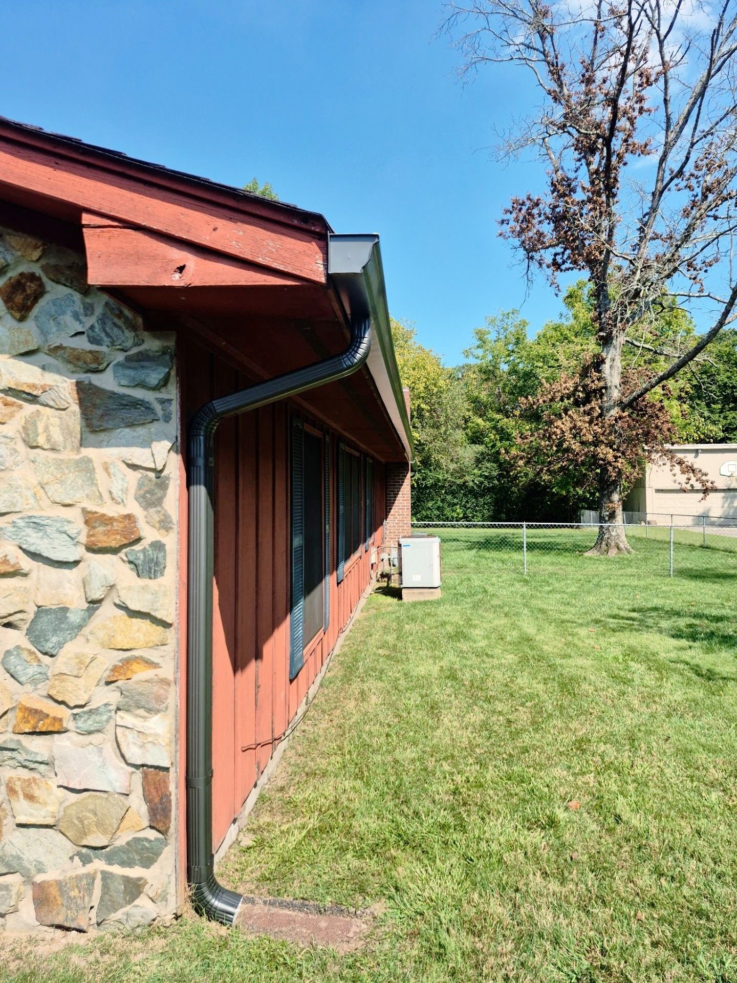 Exterior of a building with stone and red siding, black gutters, and a grassy lawn under a blue sky.