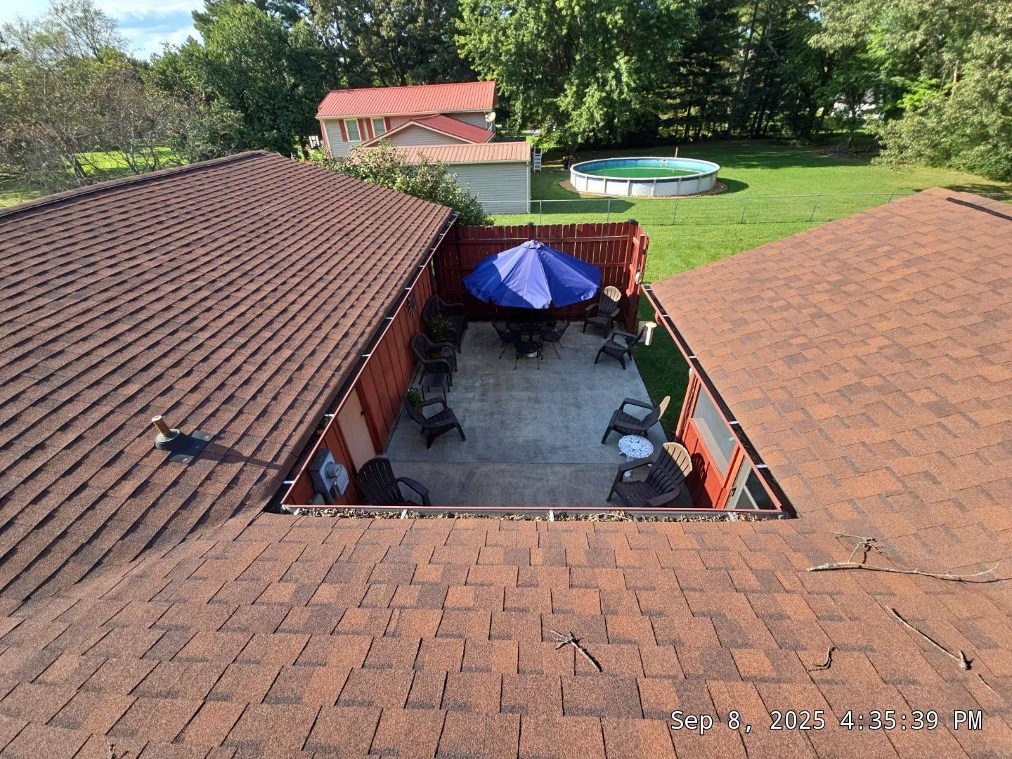Overhead view of a patio with furniture, umbrella, and a pool in the background, surrounded by a brown shingled roof.