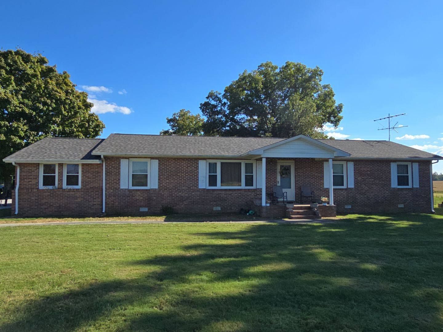 Brick ranch house with white trim, set on a green lawn under a blue sky.
