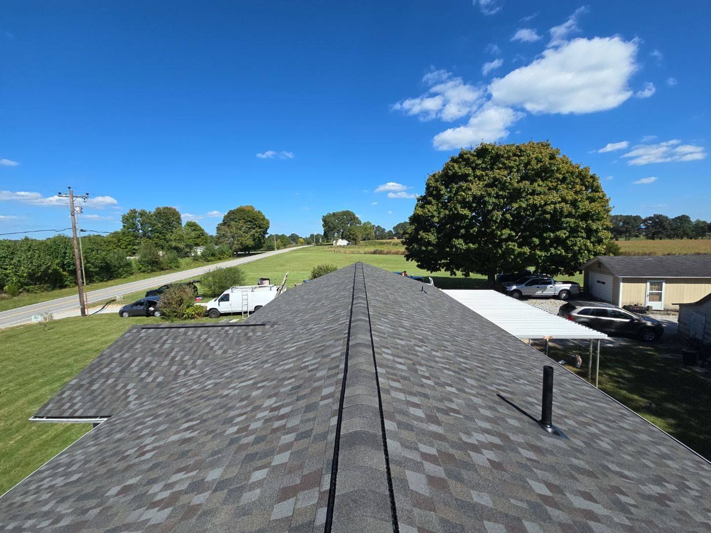 View from a roof of new gray shingles with a centered ridge vent and clear blue sky in the background.