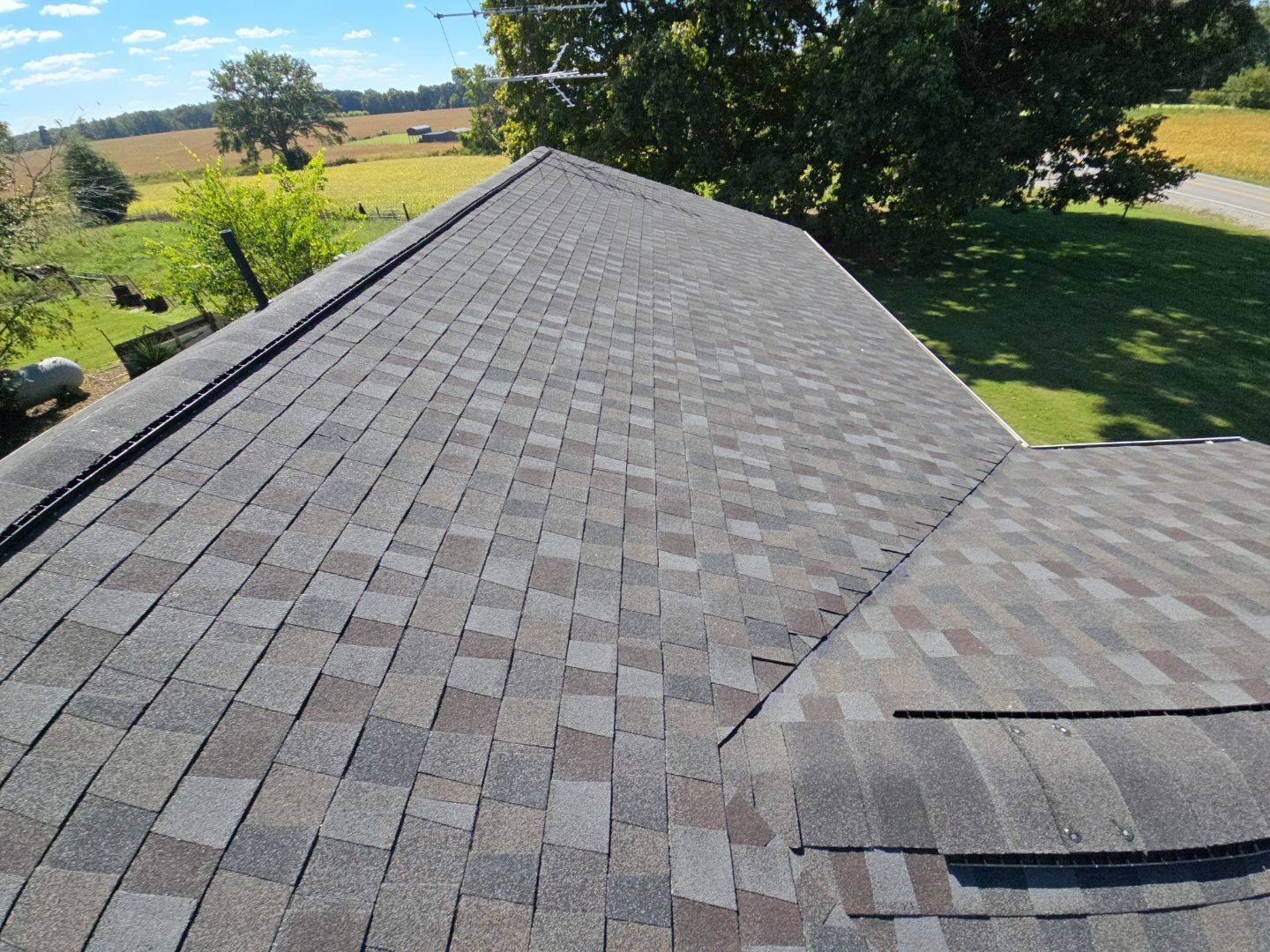 Close-up of a multi-tone shingle roof with an aerial view of the surrounding landscape.