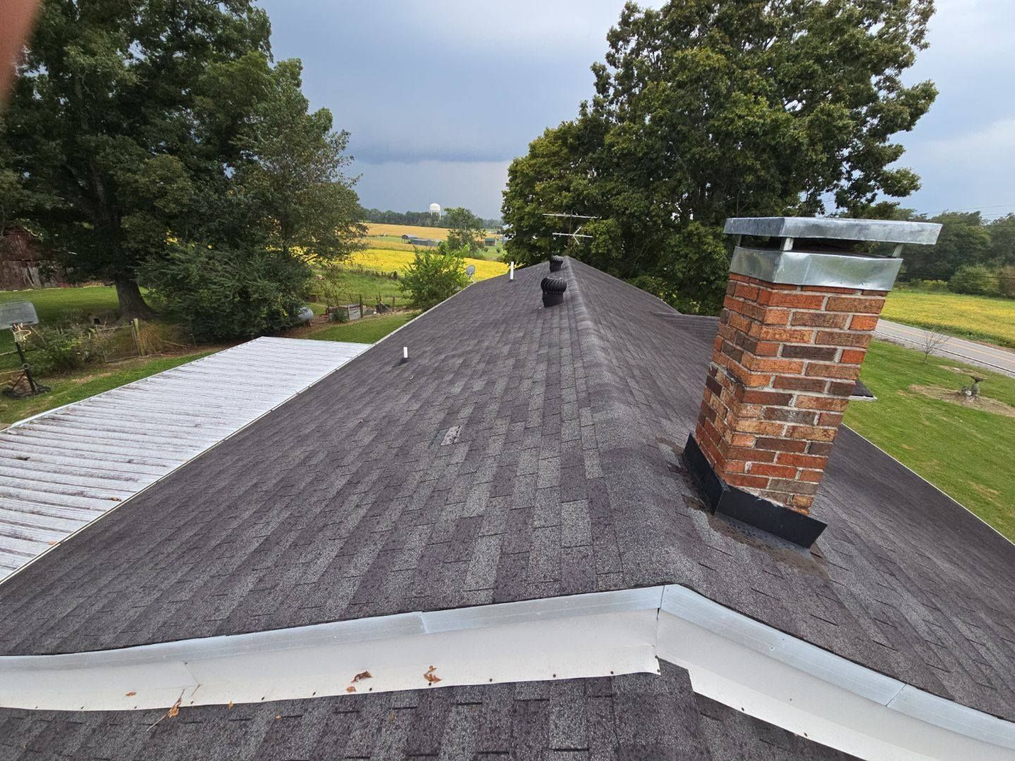 Roof of a house with gray shingles, a brick chimney, and a dark sky.