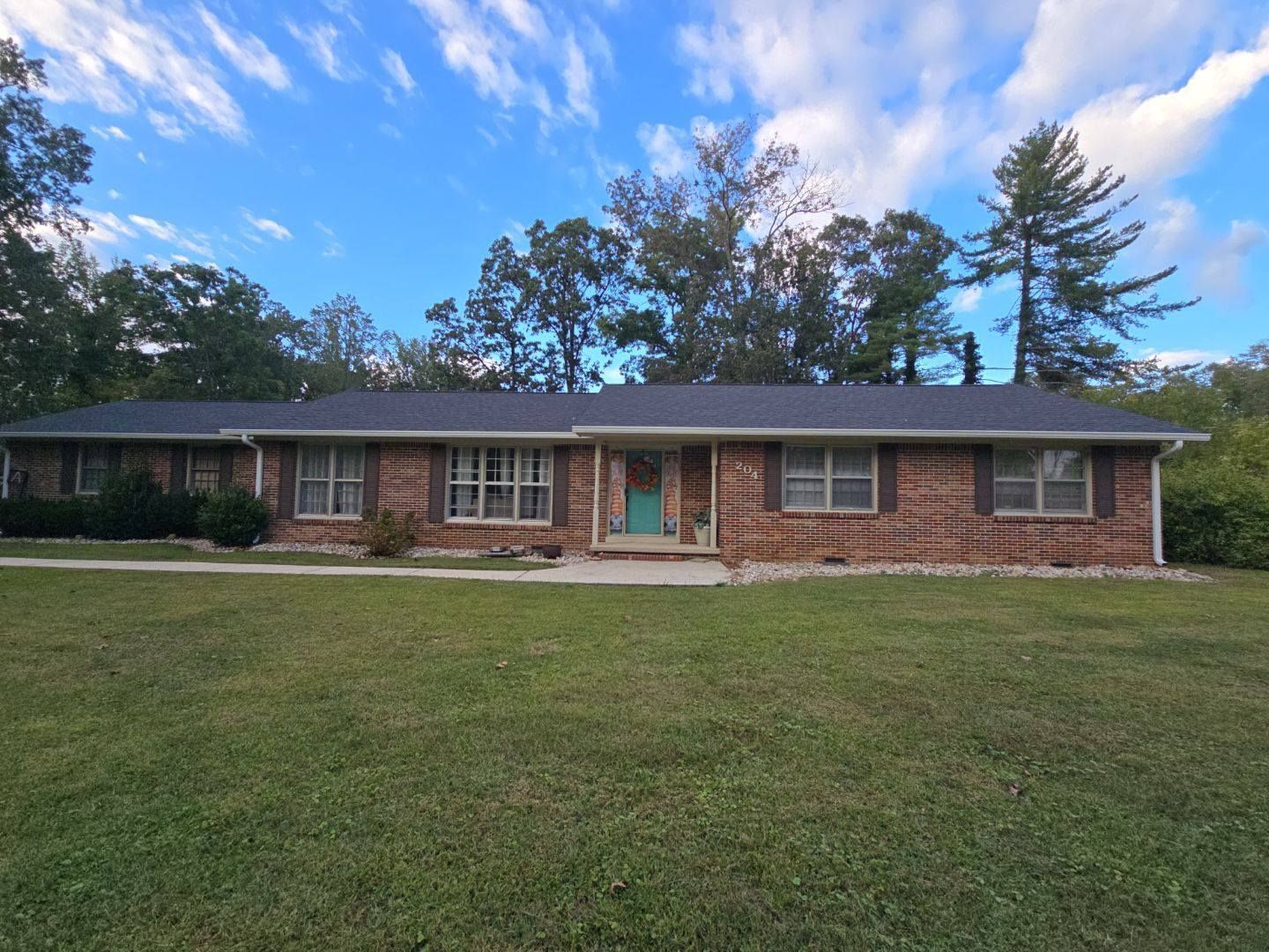 Brick ranch-style house with green door and brown shutters on a grassy lawn under a blue sky.