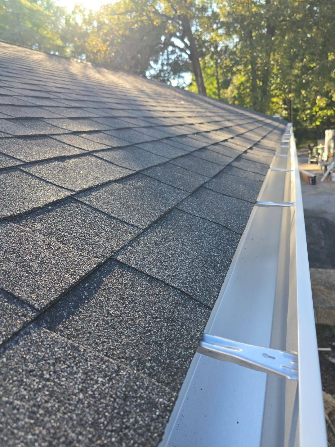 Dark asphalt shingle roof with a silver gutter attached, sunlight.