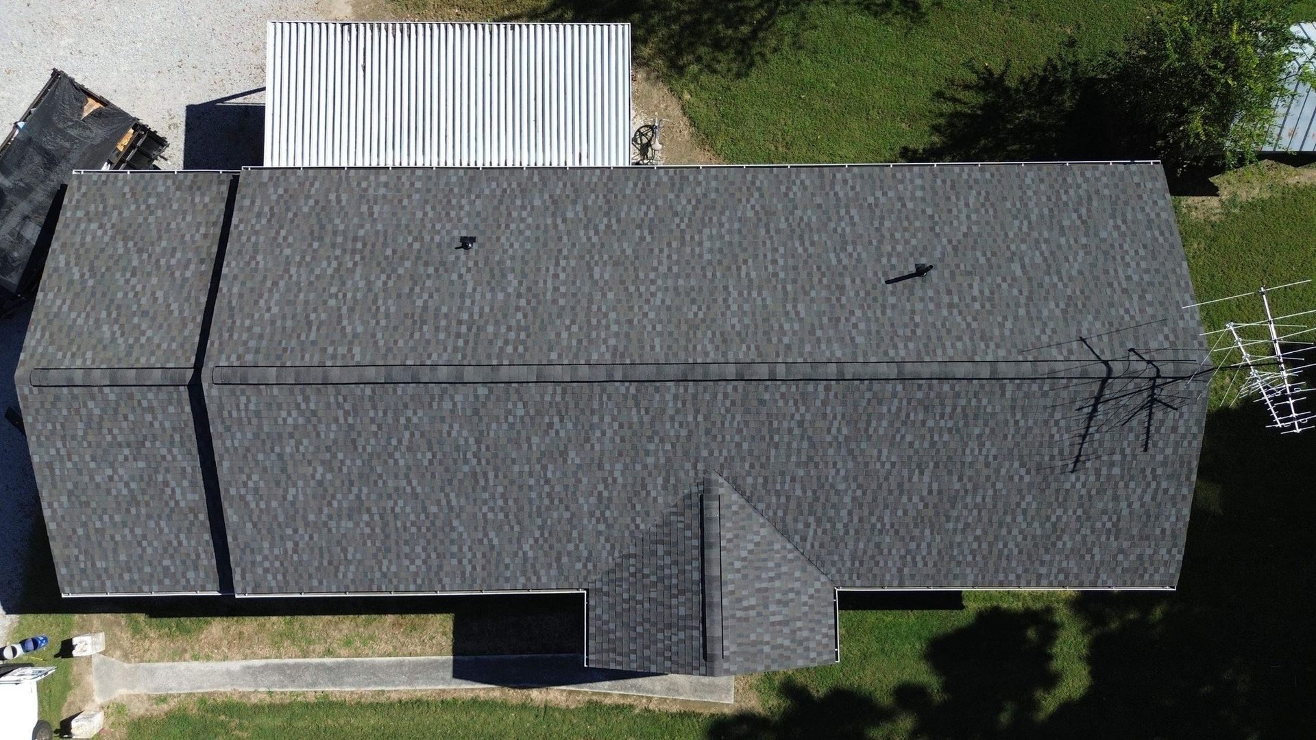 Overhead view of a house with a gray shingled roof, a small white building, and green grass.