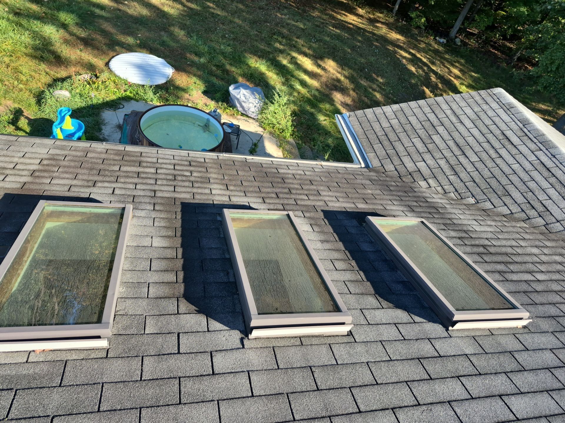 Three rectangular skylights on a weathered, shingled roof. A patio is visible in the background.