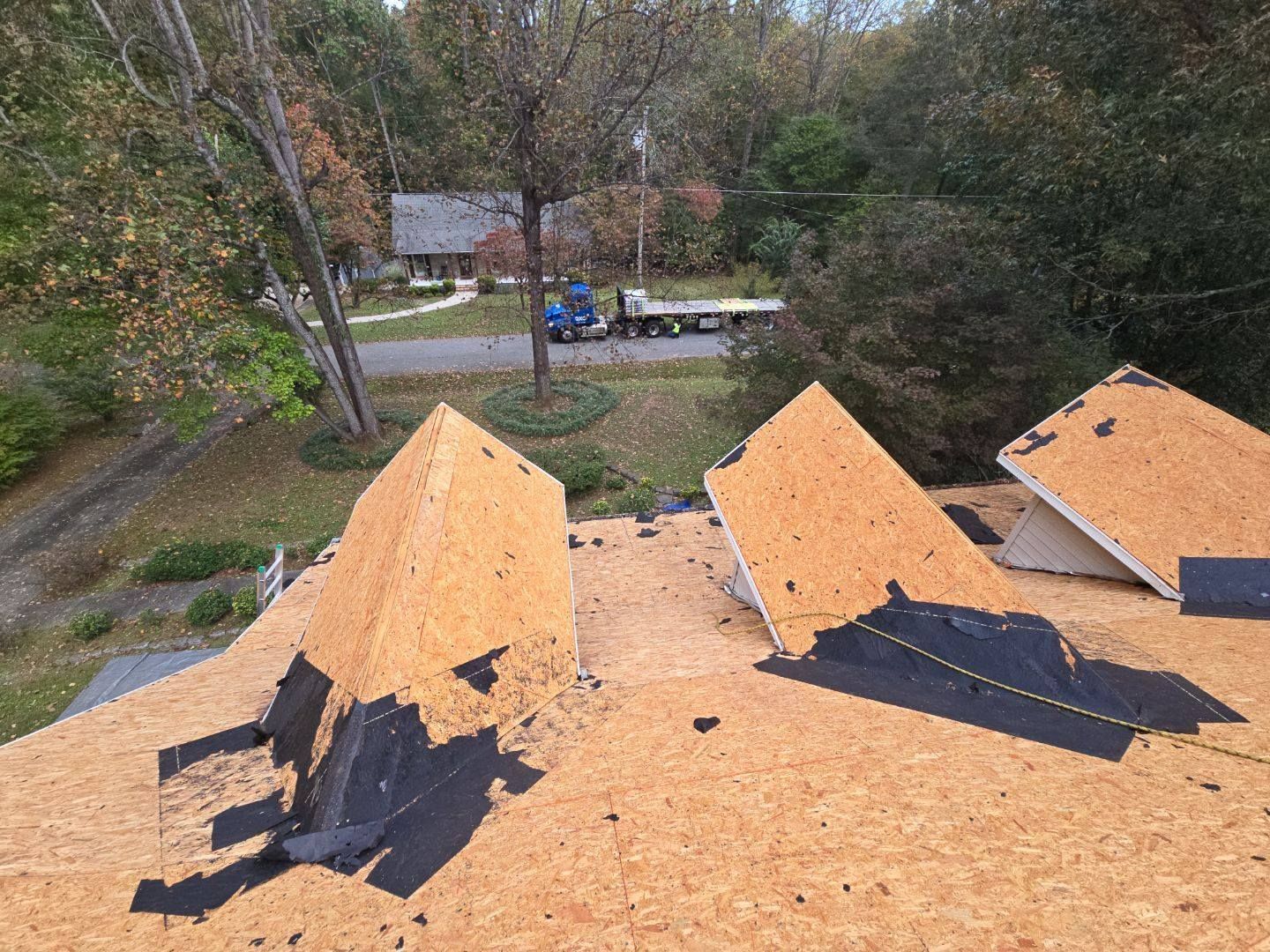 A partially dismantled roof with exposed wooden boards, viewed from above, with a truck in the distance.