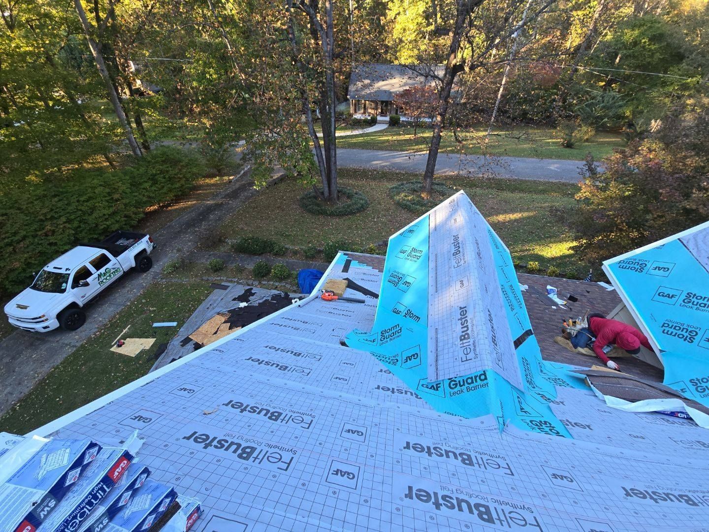 Workers installing roofing on a house; blue underlayment and truck in the background.