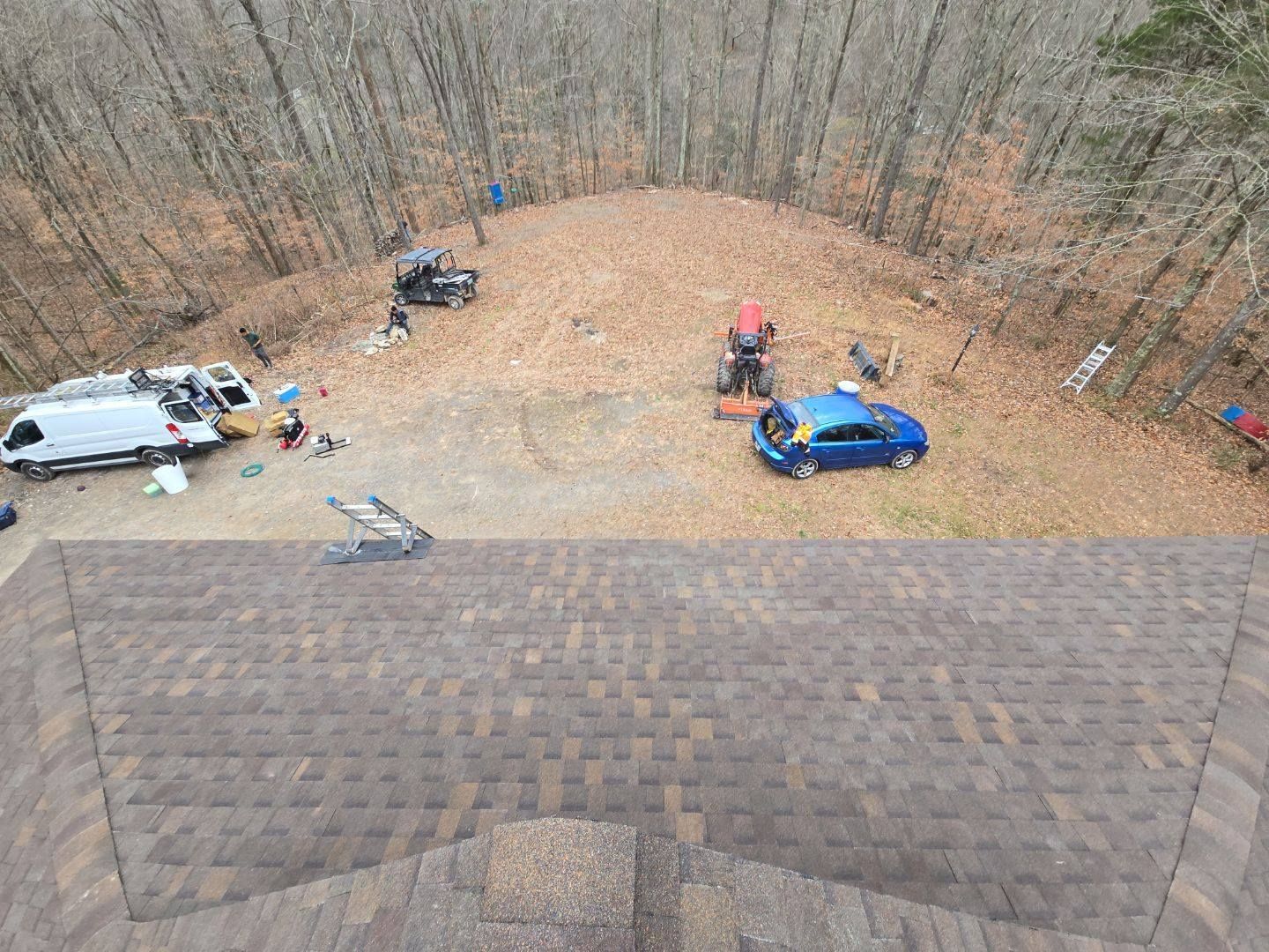 View of a roof with parked vehicles and workers on a leaf-covered hill in a wooded area.