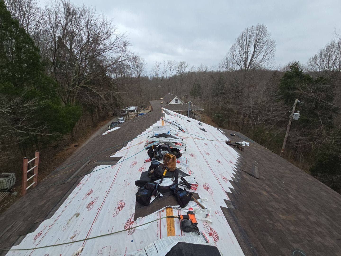 Roofers working on a house roof. White protective layer covers part of the roof. Overcast day.