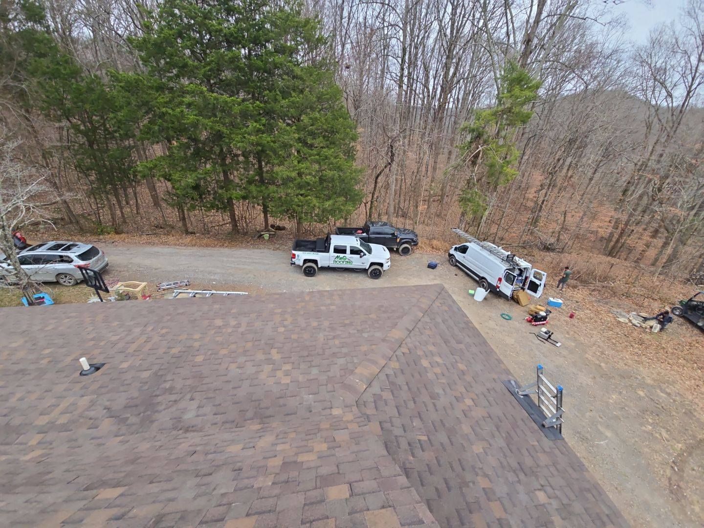 Brown roof with vehicles on a gravel driveway next to a treeline.