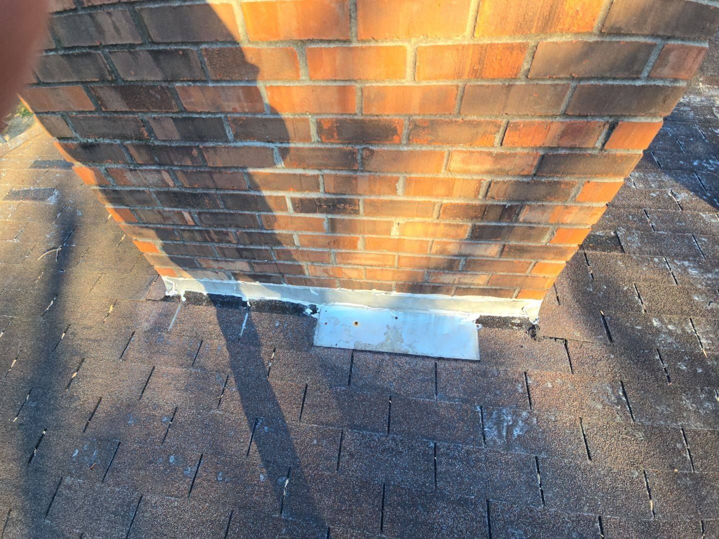 Chimney on a shingle roof with flashing visible. The bricks are reddish-brown.