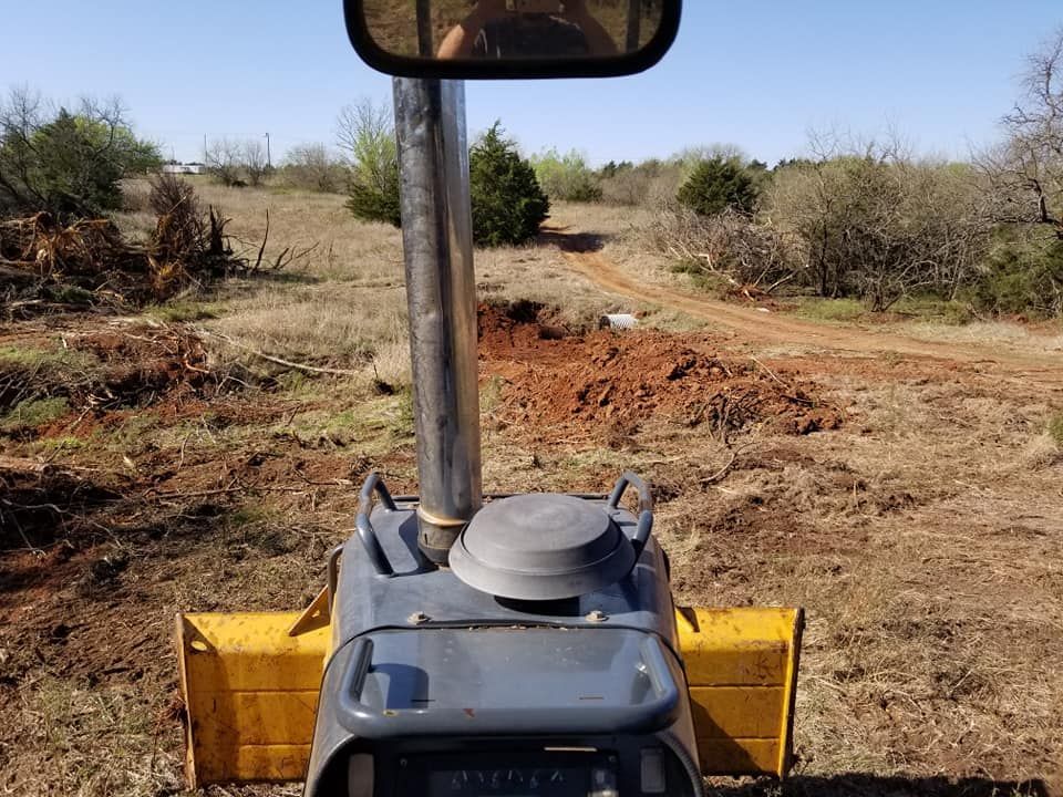 A bulldozer is driving through a dirt field with trees in the background