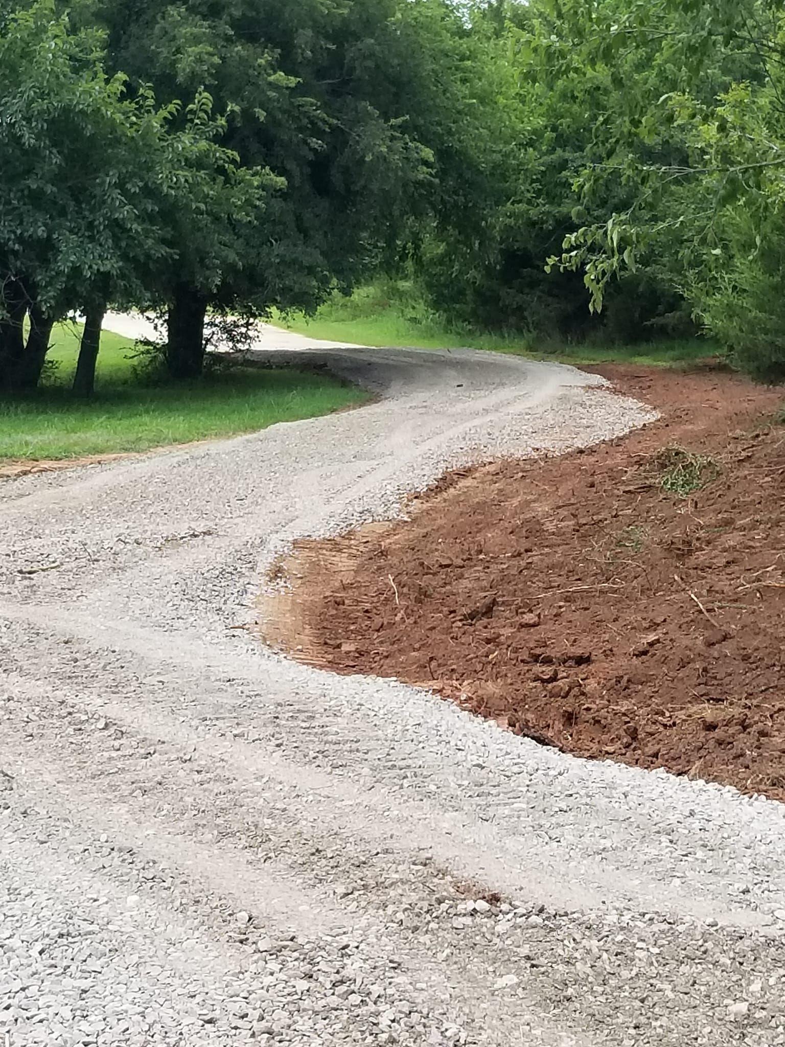 A gravel road going through a forest with trees on both sides.
