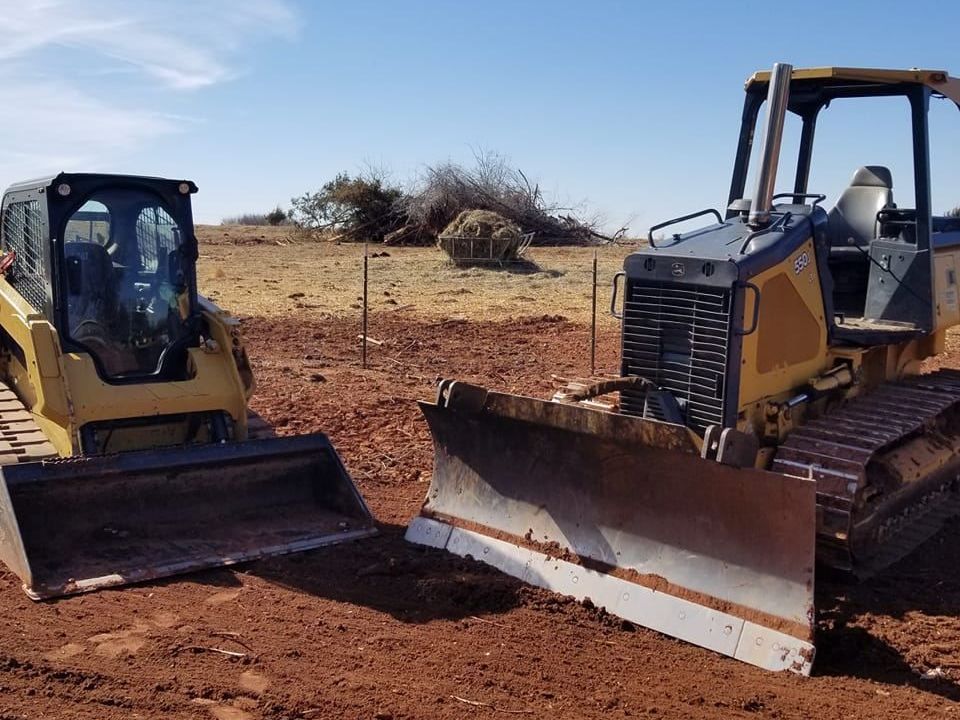 Two bulldozers are parked next to each other in a dirt field