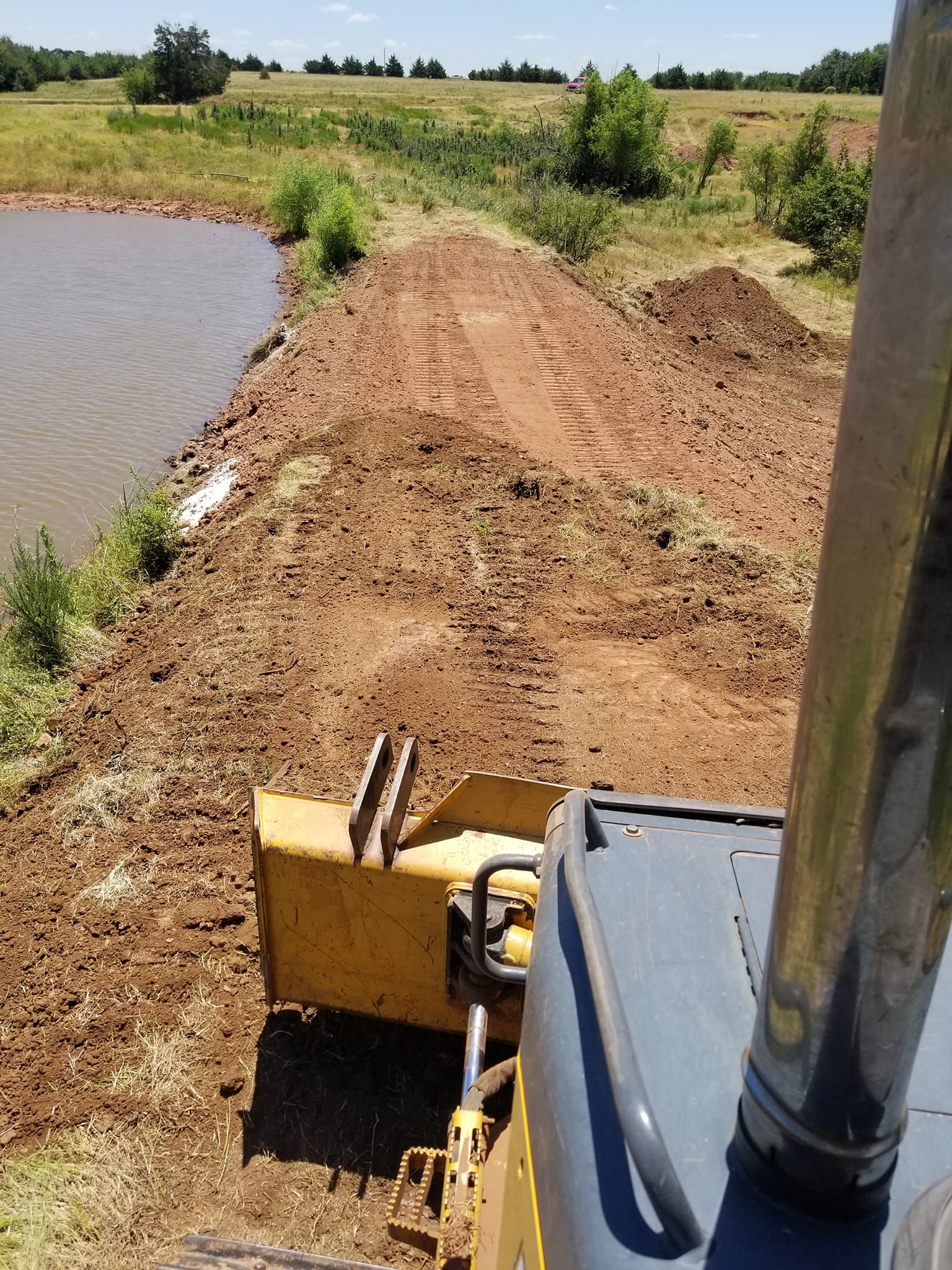 A bulldozer is working on a dirt road next to a body of water.