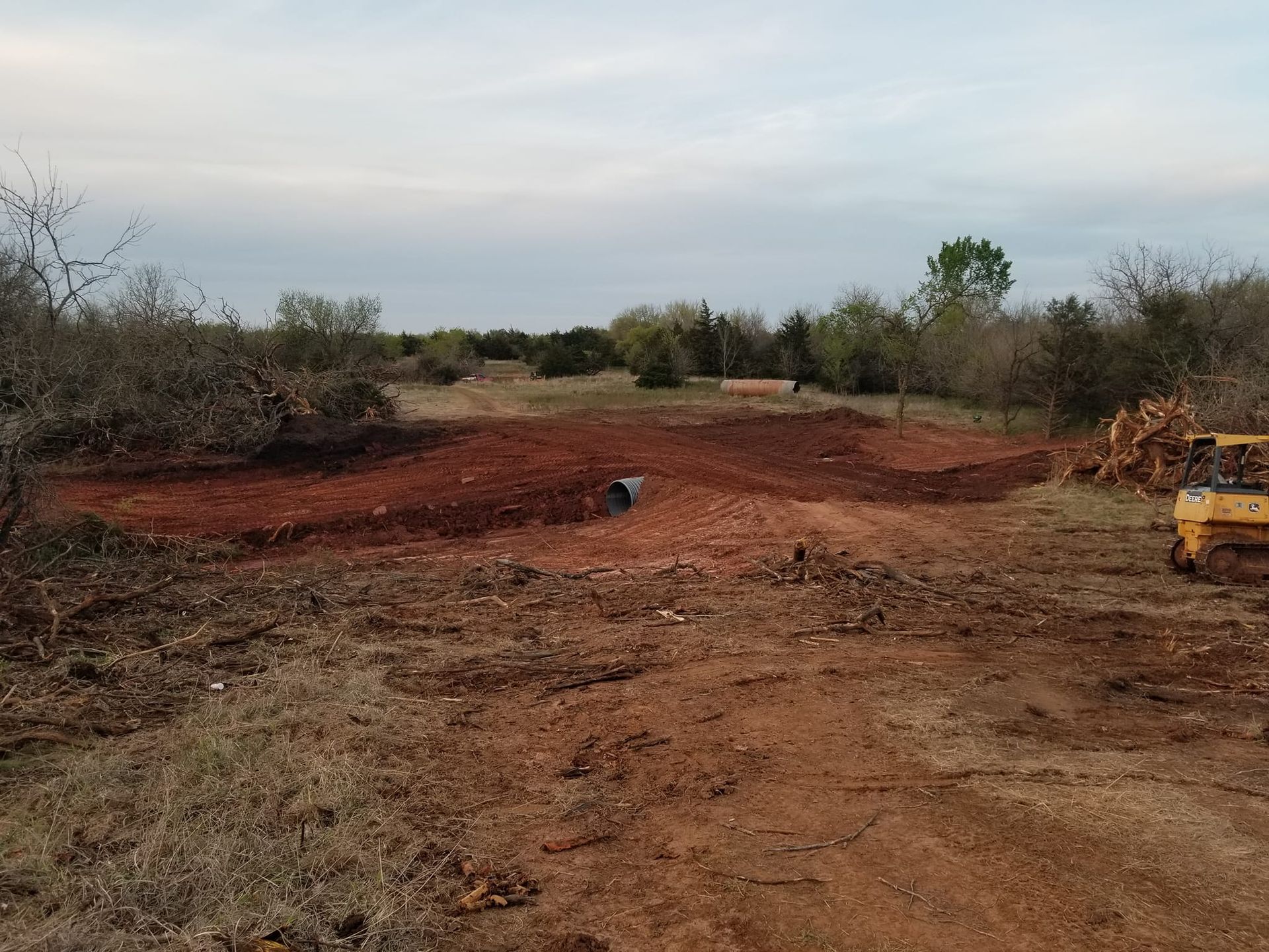A large dirt field with trees in the background and a yellow tractor in the foreground.