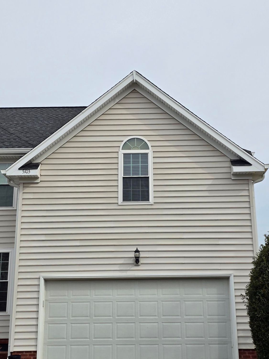Front view of a beige townhouse with a white garage and arched attic window