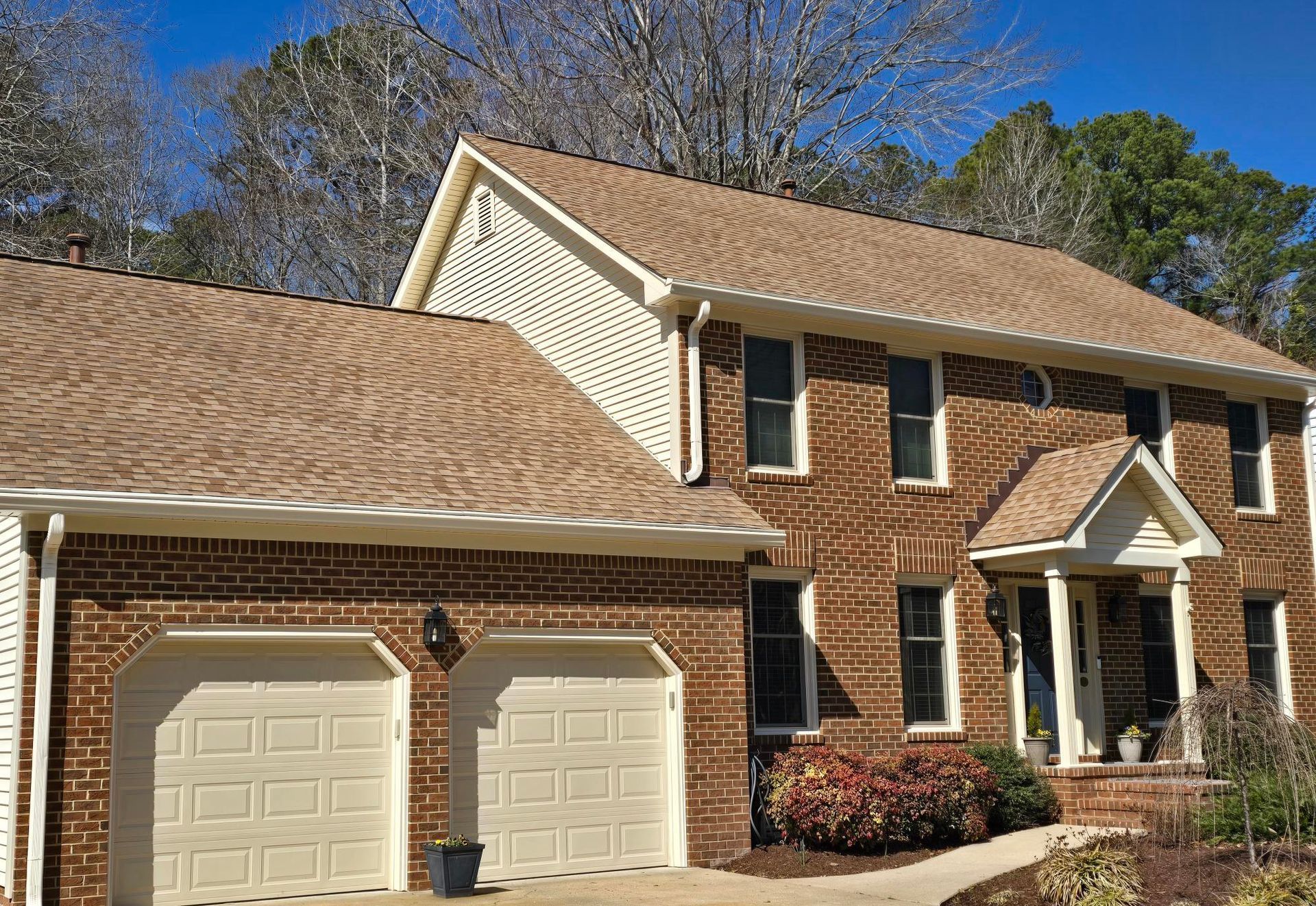 Suburban two-story brick house with two-car garage and beige siding under a blue sky
