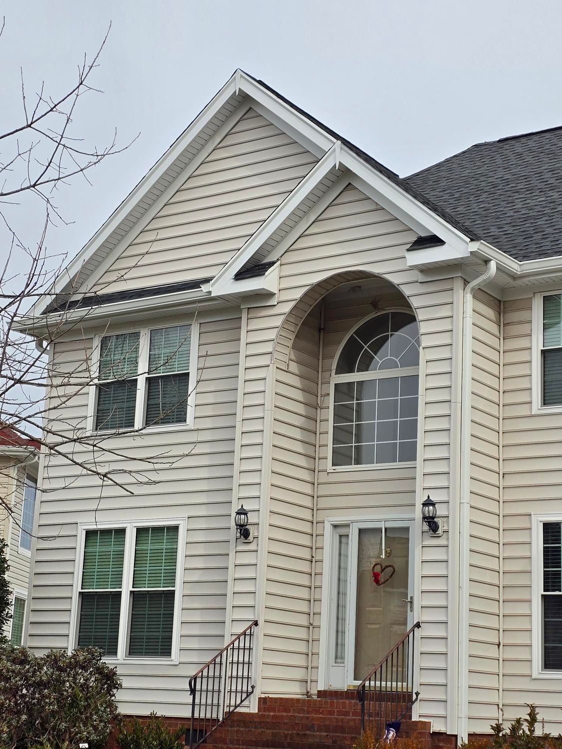 Beige two-story house with white trim, arched entry, green shutters, and a front porch with steps