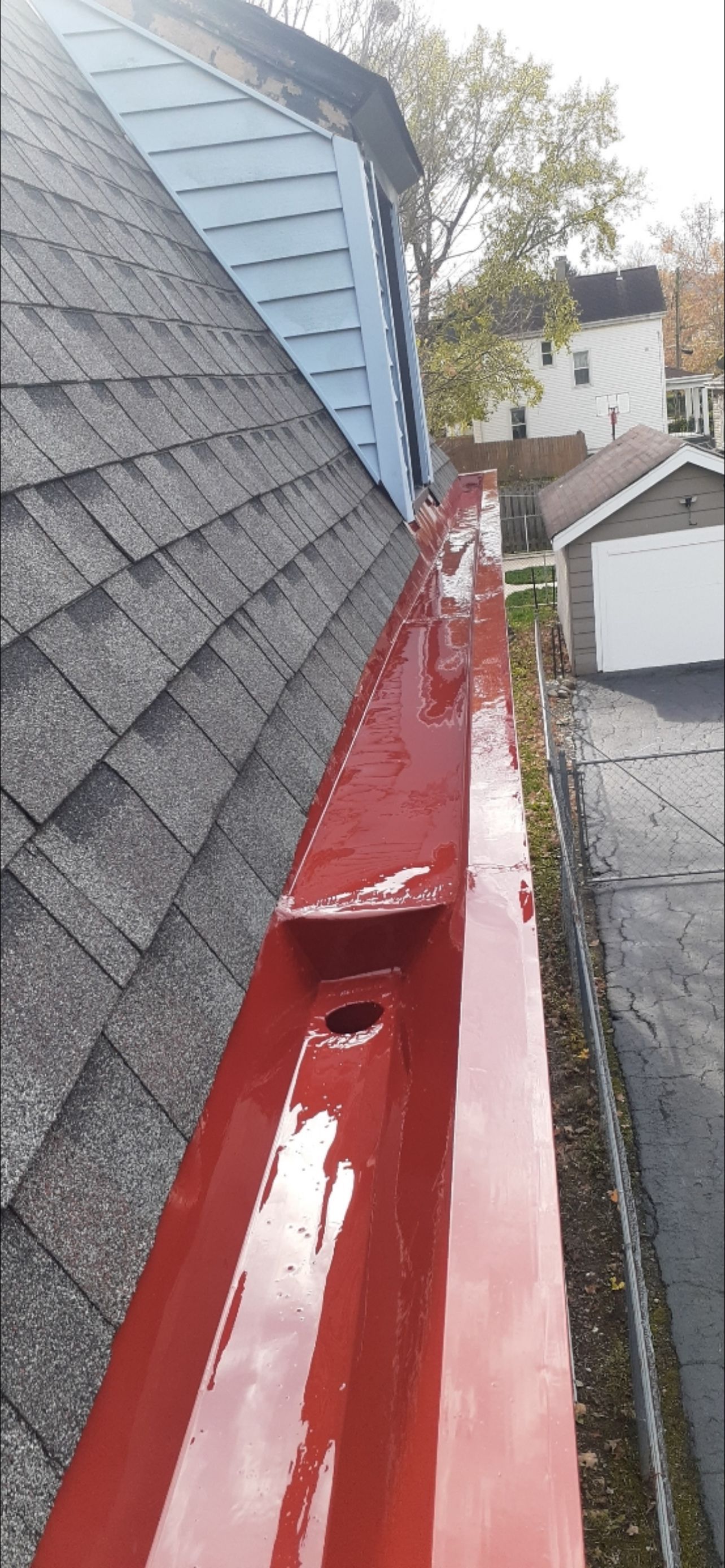 A red gutter is sitting on top of a roof next to a garage.
