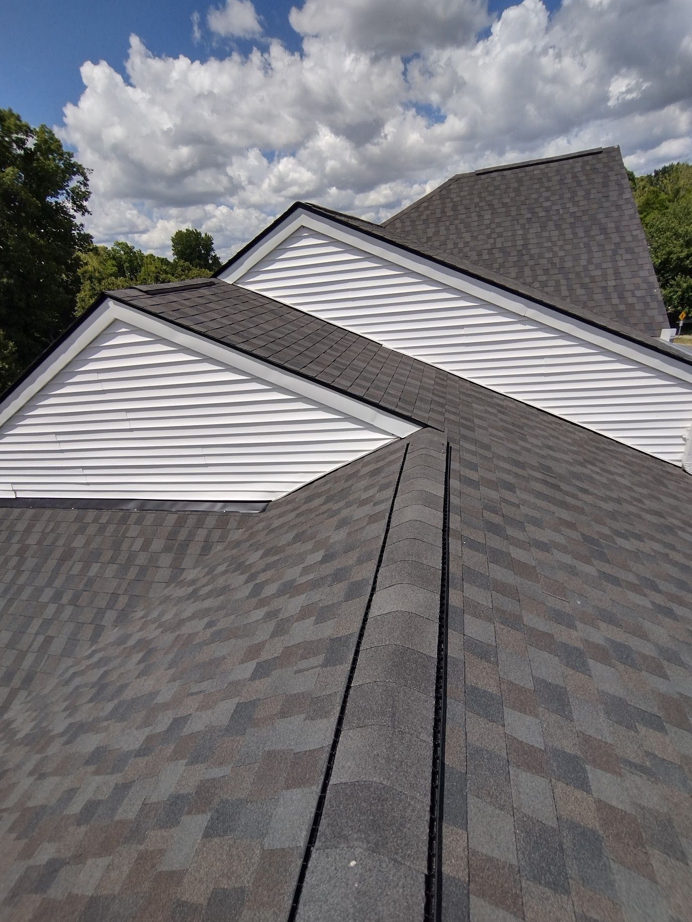The roof of a house with a gray shingle roof and white siding.