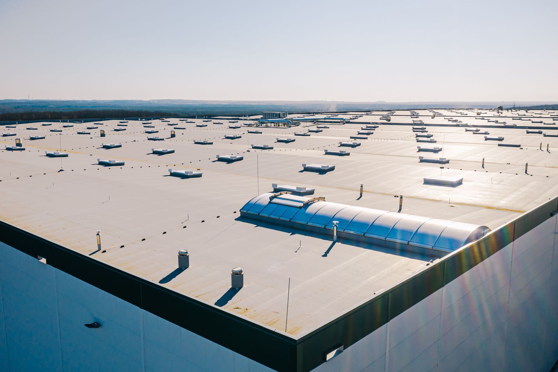 High-angle view of a vast, flat industrial building roof with numerous vents and a large, curved skylight.