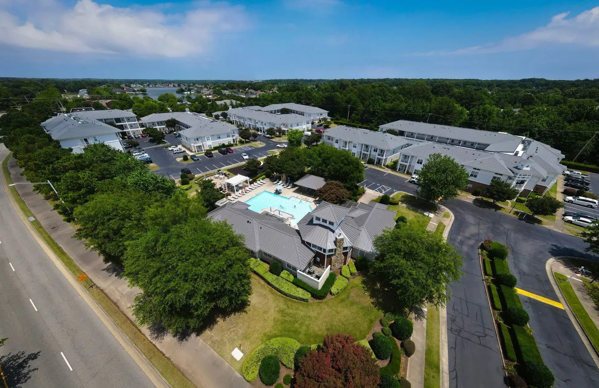 Aerial view of a residential apartment complex with a central swimming pool, surrounded by trees and a paved parking lot.