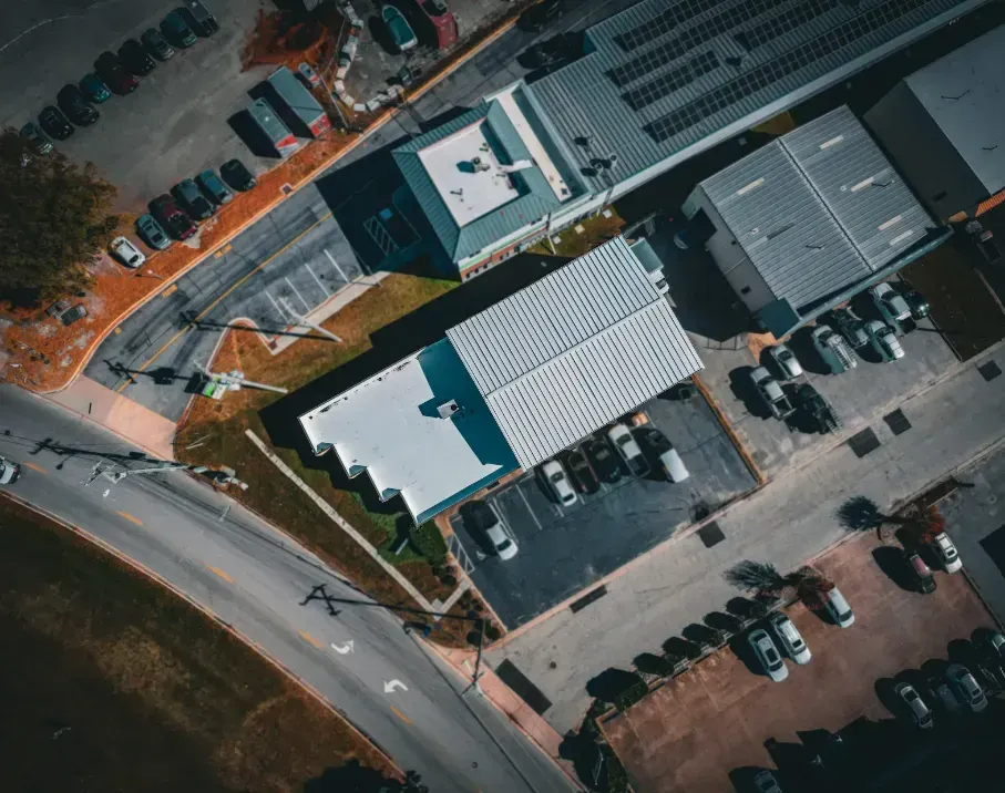 Aerial view of several commercial buildings with flat roofs surrounded by parking lots and a winding road.