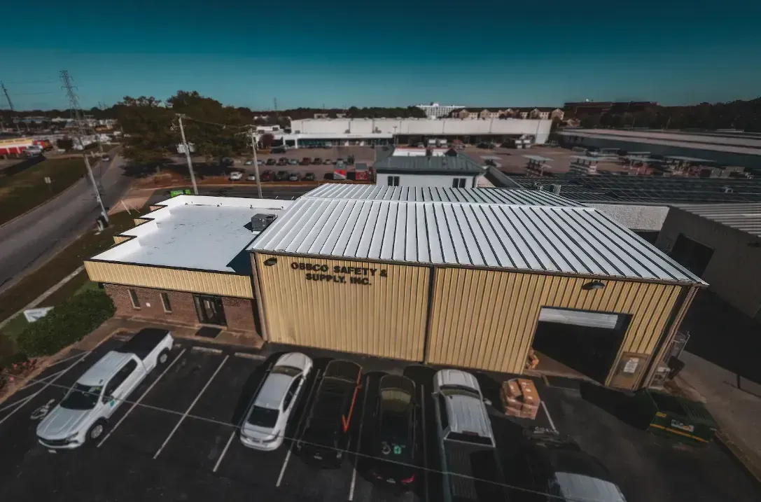 Aerial view of a yellow commercial building with a corrugated metal roof and a parking lot with parked vehicles.