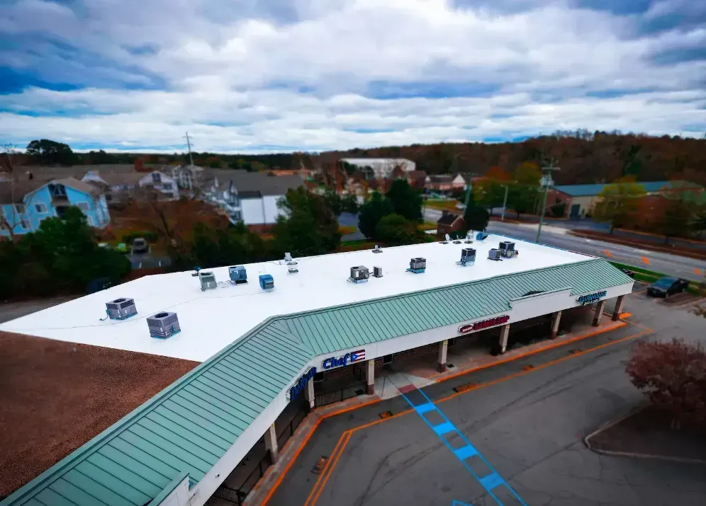 Aerial view of a commercial strip mall with a white flat roof, green metal awning, and a parking lot with blue markings.