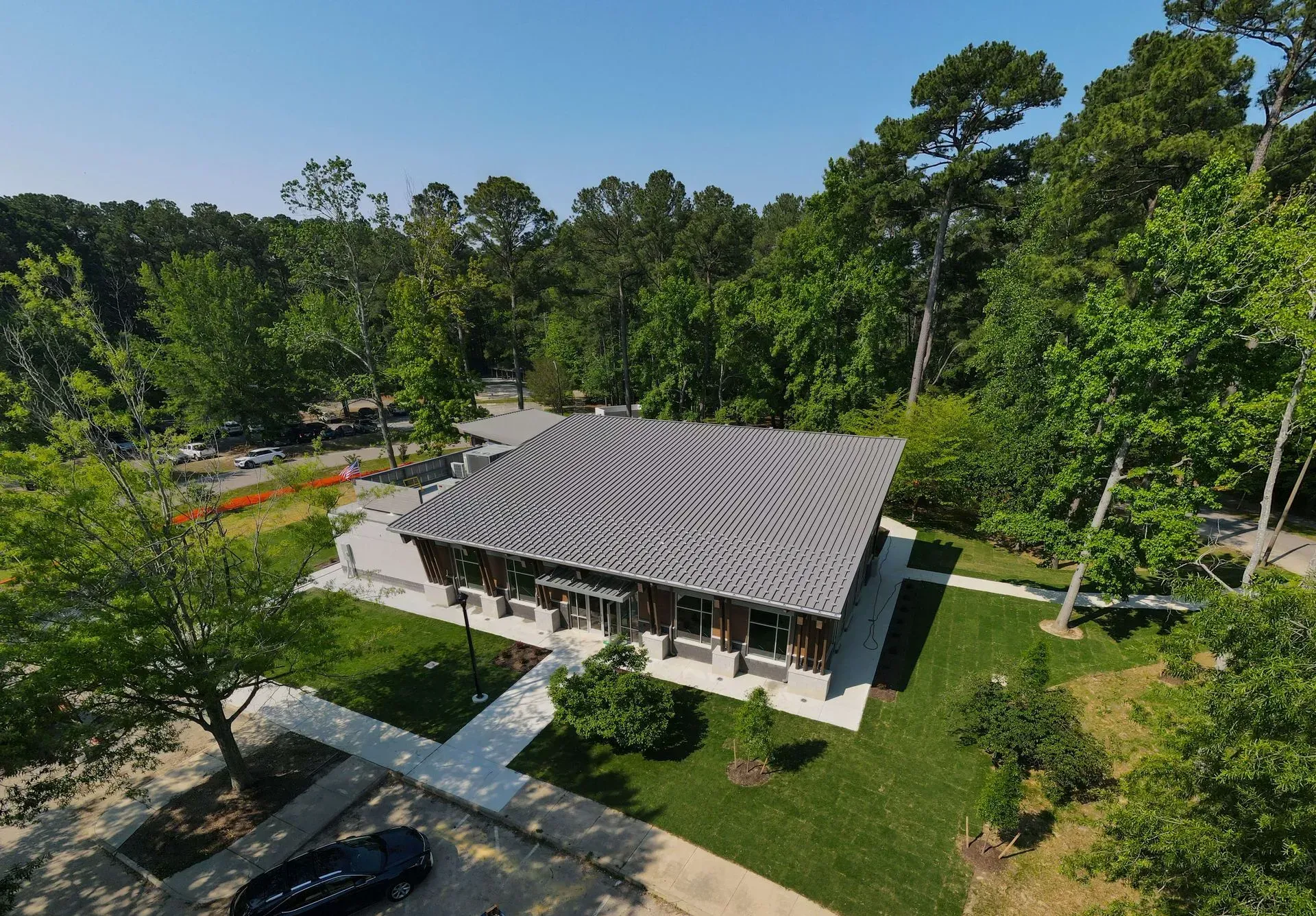 An aerial view of a single-story brick building with a dark, patterned roof surrounded by trees and paved walkways.