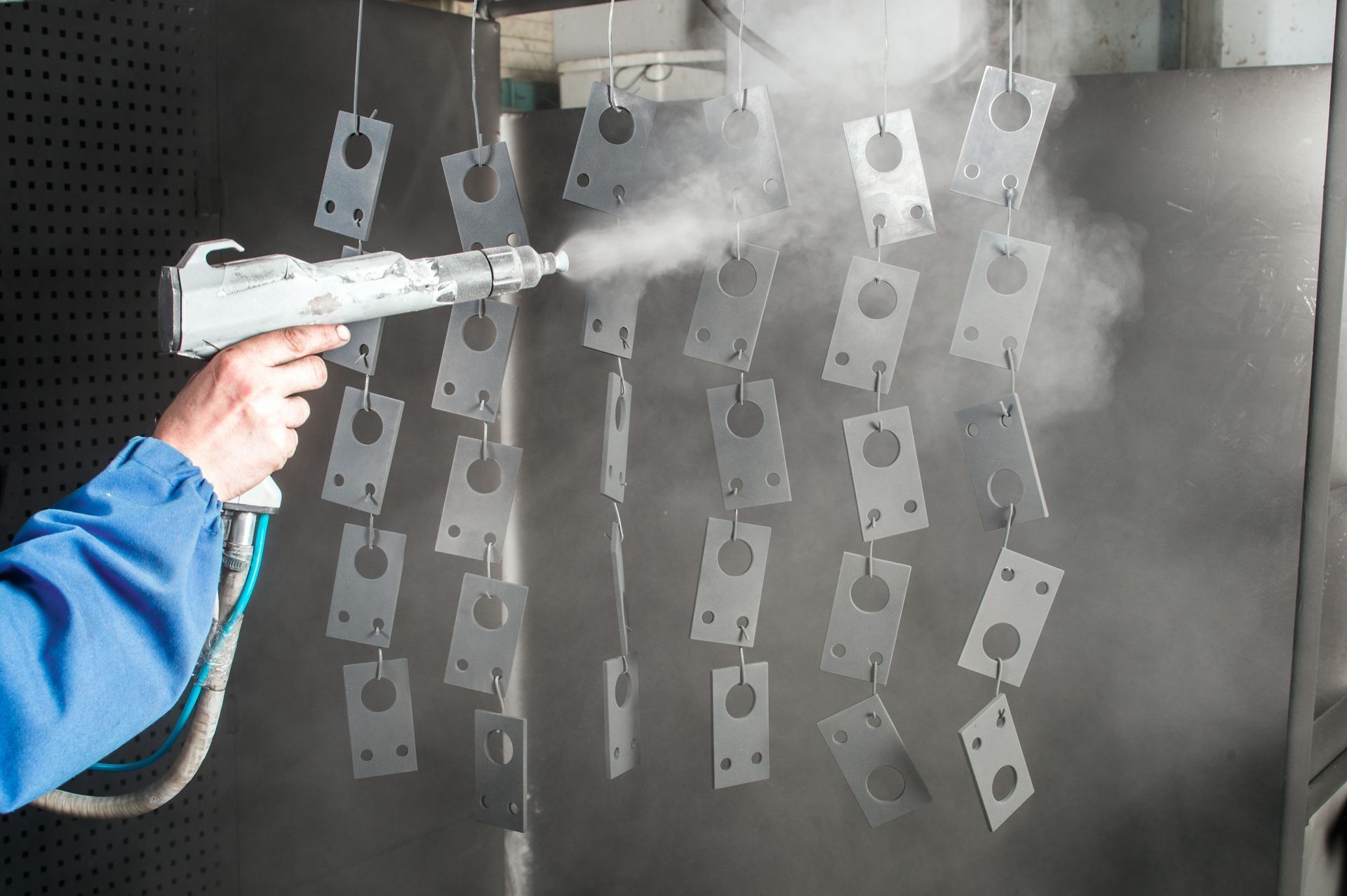 Person spray-painting metal parts with a paint gun in a workshop.