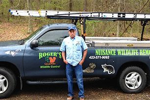 A man is standing in front of a roger 's wildlife control truck.