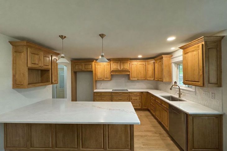 Spacious kitchen with oak cabinets, white countertops, island, and stainless sink under recessed lights.