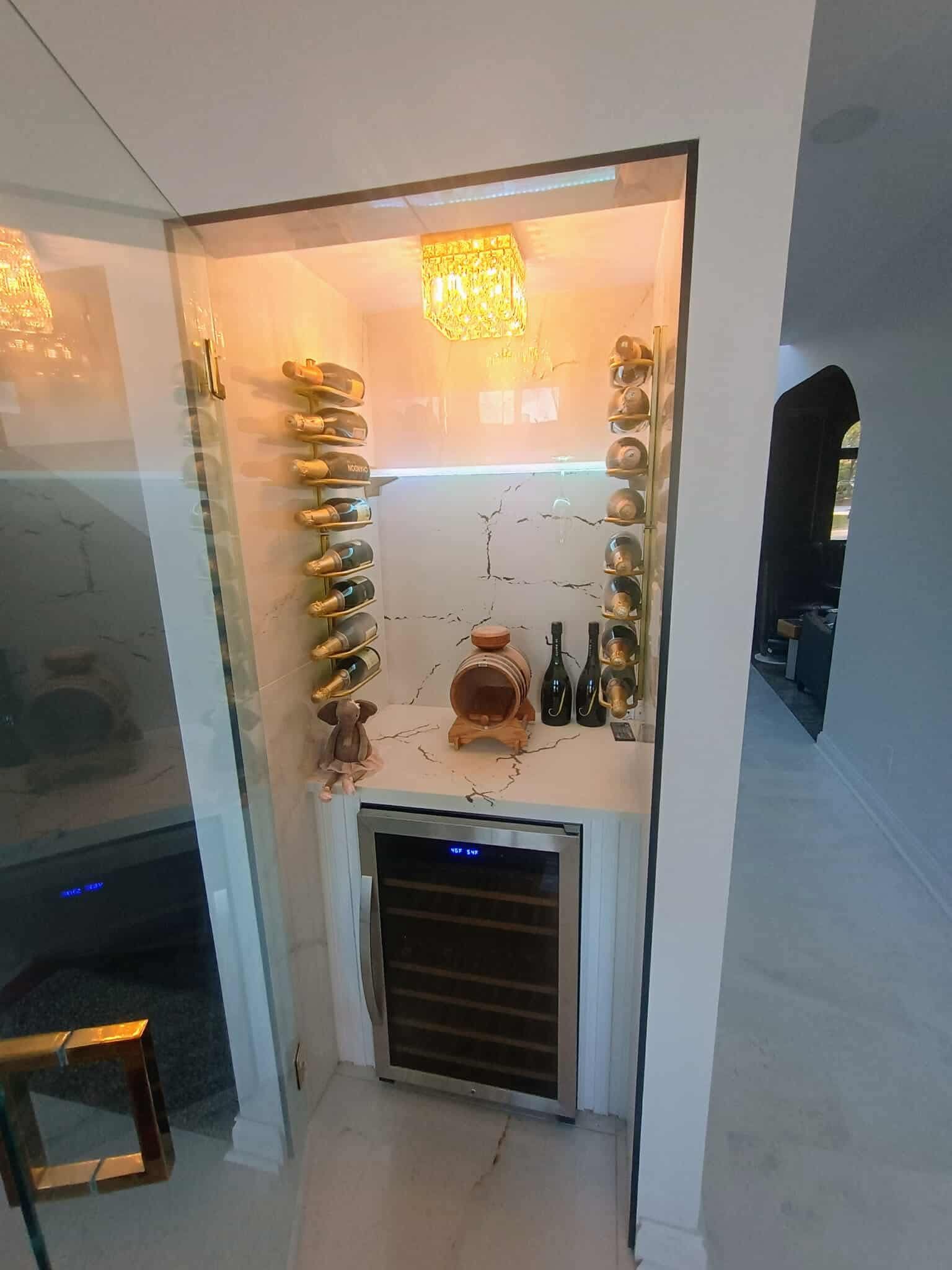 Wine display nook with stacked bottles, warm lighting, and a small wine cooler below