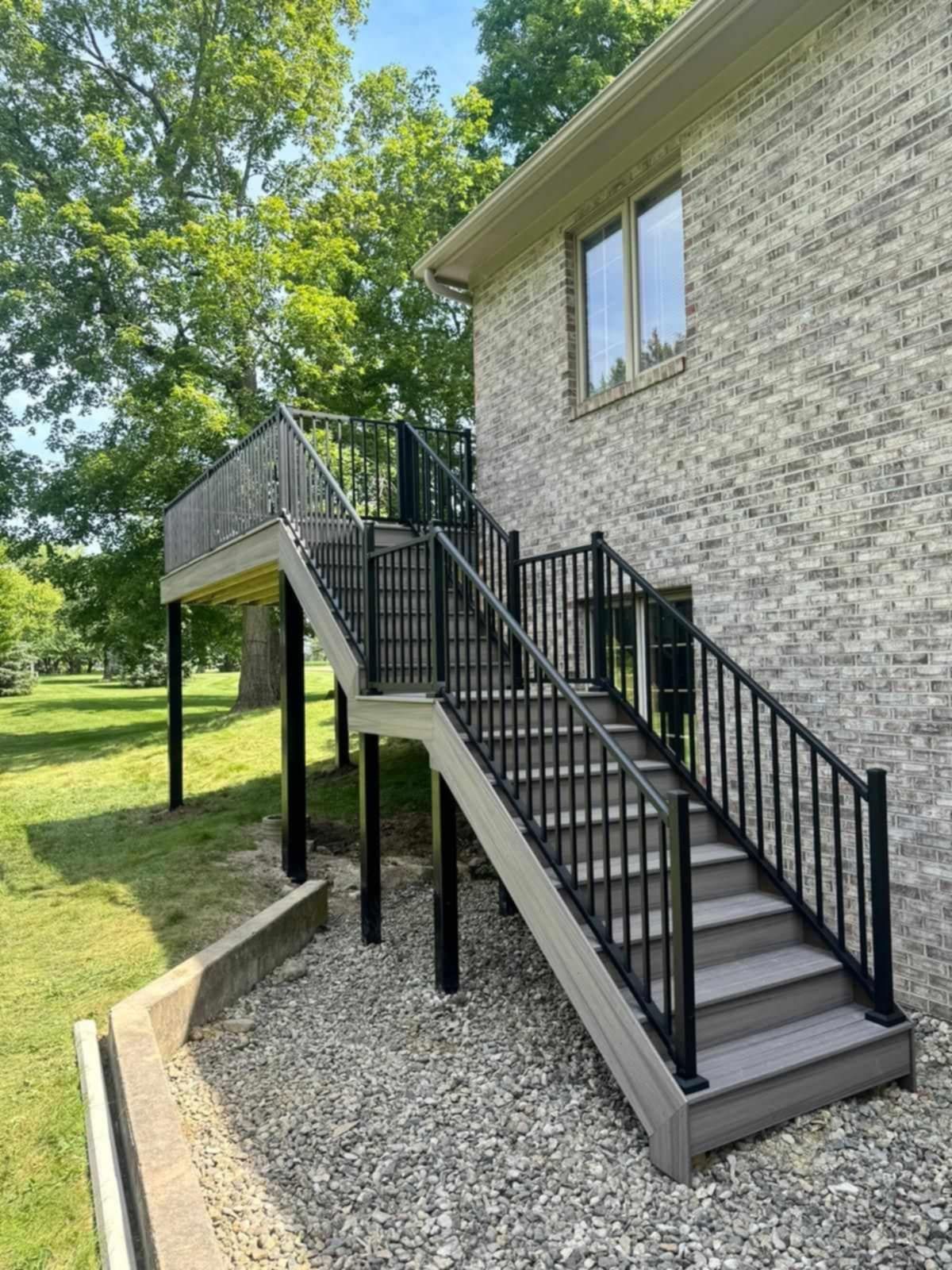 Side view of a brick house with an exterior staircase, black railings, and gravel landscaping.