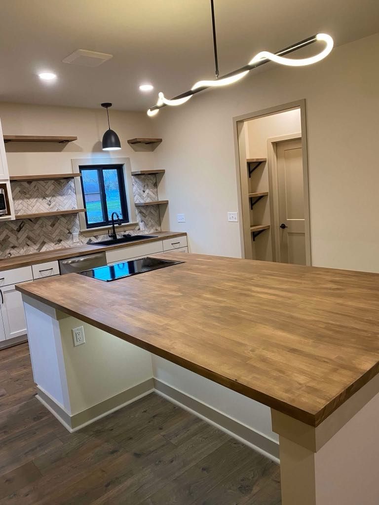 Modern kitchen with a large wood island, white cabinets, pendant lights, and a pantry doorway.